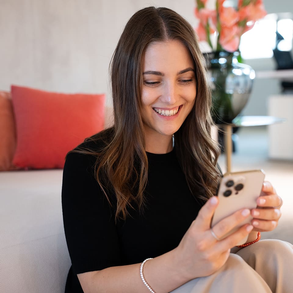 Mitarbeiterin der Influencer Agency BUZZINTALENTS sitzt in moderner Lounge und blickt lächelnd auf ihr Smartphone.